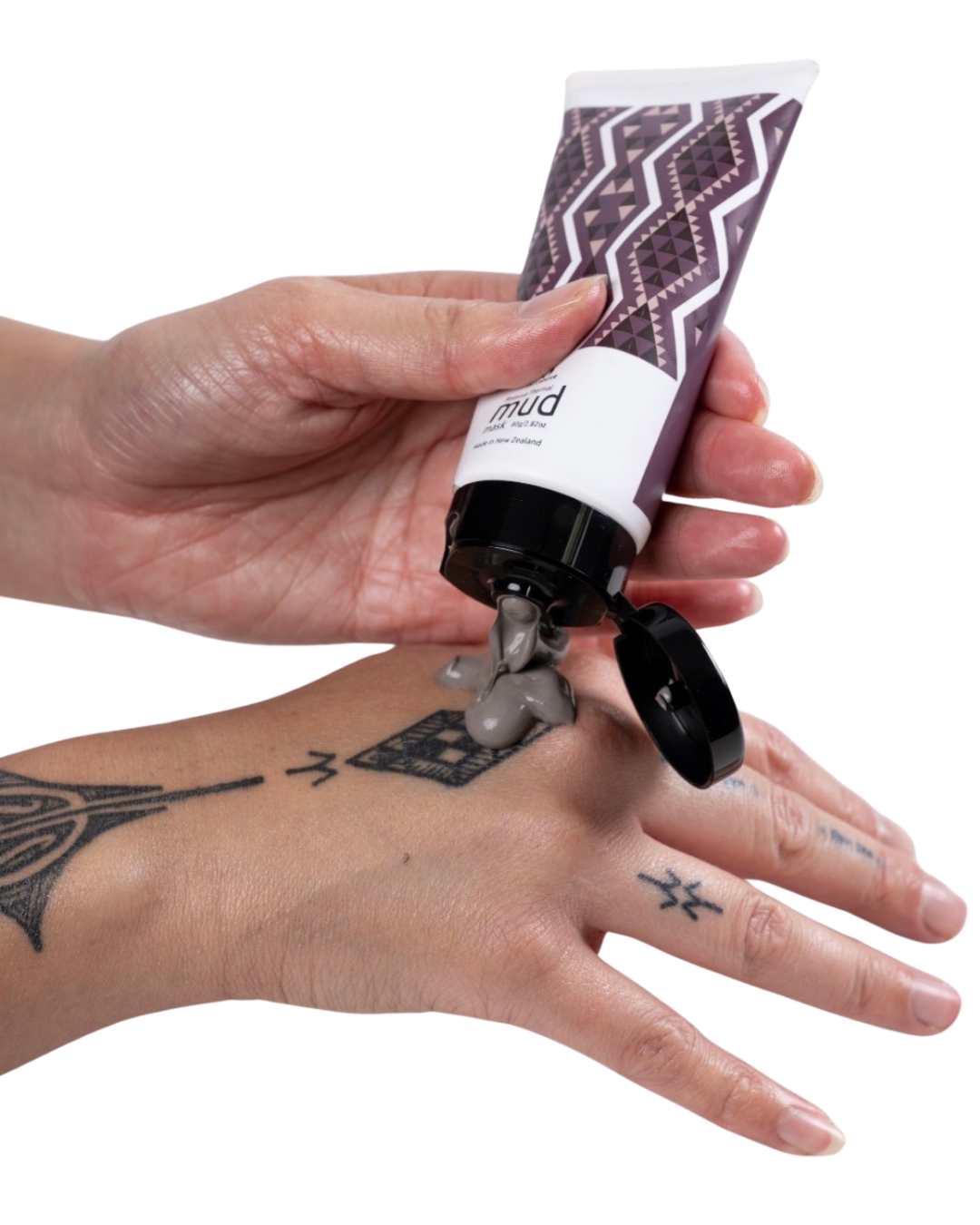 Hand applying a tube of Rotorua's Pure Source Geothermal Mud to another hand with Māori tattoos on a white background. Tube is decorated with Ahu Boutique's design in purple and brown tones.